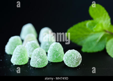 Close up of green, gelée de menthe avec gouttes de cristaux de sucre et de feuilles de menthe douce sur un fond noir Banque D'Images