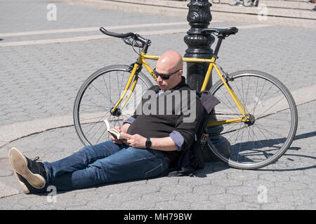 Un homme est assis en lisant un livre et se penchant sur son vélo sur une chaude journée de printemps. Dans la région de Union Square Park à Manhattan, New York City. Banque D'Images