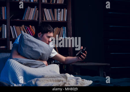 Image de l'homme avec l'insomnie assis au lit avec réveil Banque D'Images