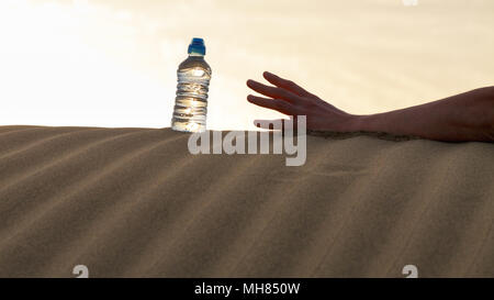 Essayez d'attraper la main l'eau de la bouteille sur le sable désert à haute température. Concept de mourir de soif. Banque D'Images