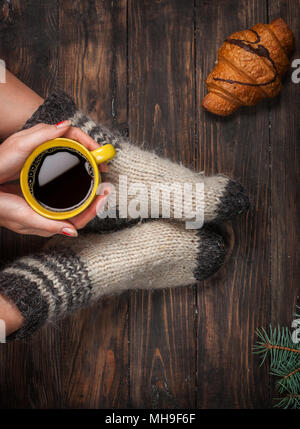 Les jambes de fille en bas de laine chaude et une tasse de café au matin d'hiver, réchauffement de la maison. Banque D'Images