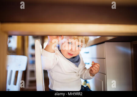 Cute toddler boy eating sweets sous la table. Banque D'Images