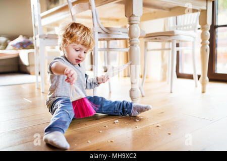 Un bébé garçon avec un balai et un porte-poussière à la maison. Banque D'Images