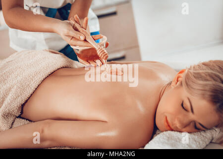 Belle jeune femme couchée et massage du dos sains avec du miel par des thérapeutes au centre de spa. Banque D'Images