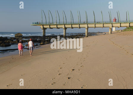 Durban, le KwaZulu-Natal, Afrique du Sud, l'adulte en train de marcher sur la plage d'Umhlanga Rocks tôt le matin vers la jetée et le phare historique Banque D'Images