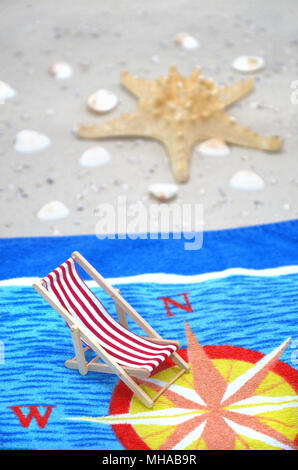 Serviette sur la plage avec une étoile de mer, coquillages, et une chaise Banque D'Images