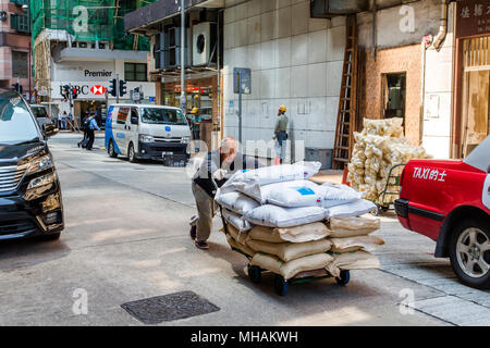 Un vieil homme asiatique pousse un chariot chargé avec des sacs de marchandises grâce à une rue de l'île de Hong Kong. Certains sacs sont marqués comme produit des États-Unis Banque D'Images