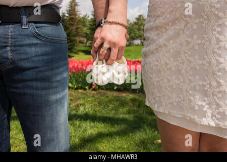 La femme enceinte attend son bébé. Cette photographie prend alors qu'elle tenait des chaussures dans sa main devant des fleurs et un lac. Banque D'Images