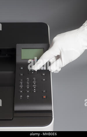 Woman's hands en gant blanc appui bouton sur le panneau de commande de l'imprimante laser couleur sur gris Banque D'Images