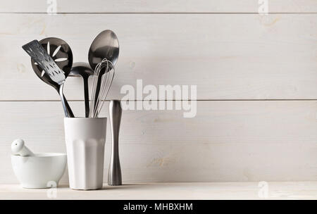 Des ustensiles de cuisine dans la tasse blanche avec un pilon et mortier sur tableau blanc avec fond en bois blanc Banque D'Images