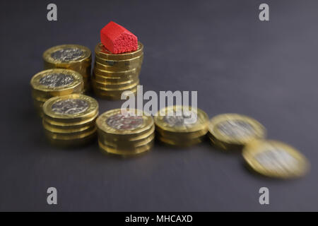 Modèle rouge d'une maison en haut d'une pile de pièces d'une livre Banque D'Images