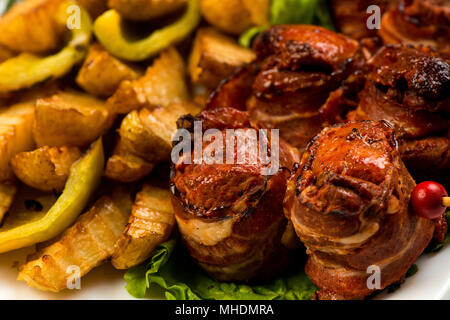 Rouleaux de bacon et d'une viande grillée avec frites et sauce rouge sur plaque blanche sur fond blanc Banque D'Images