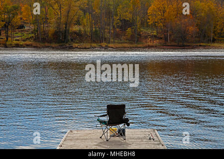 La canne à pêche s'appuie sur une chaise de camping sur un quai au bord du lac à l'automne Banque D'Images