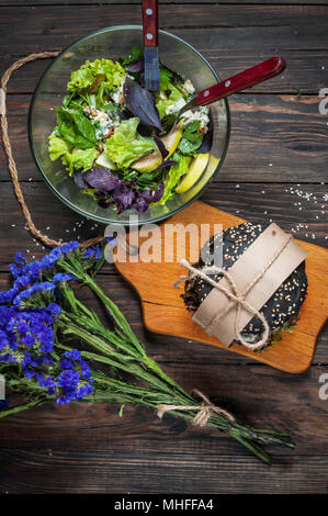 De délicieux hamburgers, salades et noir fleurs bleu foncé sur la table en bois. Banque D'Images