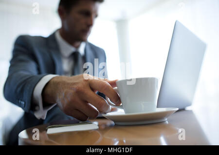 Businessman cueillette à la main une tasse de café sur une table dans office hall. Entrepreneur travaillant sur ordinateur portable et boire du café. L'accent sur l'homme hands holding coffe Banque D'Images