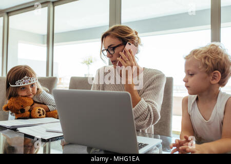 Young Woman talking on mobile phone alors qu'il était assis à l'ordinateur portable et tablette avec ses enfants. Travail de la maison mère avec ses enfants par séance. Banque D'Images
