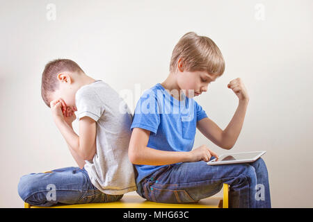 Les enfants jouer à des jeux sur ordinateur avec l'ordinateur tablette. Gagner le jeu d'un garçon et d'autres assis fatigué et malheureux après avoir perdu jeu. Banque D'Images