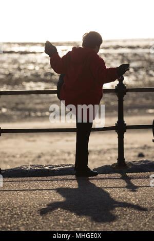 Une vieille femme chinoise faire tôt le matin, l'exercice de tai chi en utilisant les rampes sur la promenade du bord de mer pour l'appui à Llandudno, au Pays de Galles Banque D'Images