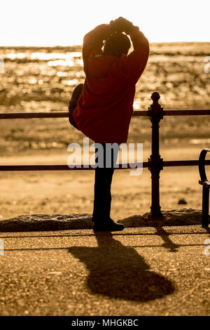 Une vieille femme chinoise faire tôt le matin, l'exercice de tai chi en utilisant les rampes sur la promenade du bord de mer pour l'appui à Llandudno, au Pays de Galles Banque D'Images