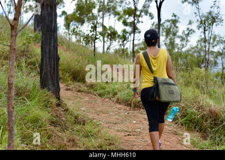 La Marche des femmes avec des vêtements de sport et une bouteille d'eau sur un chemin forestier, Mount Stuart des sentiers de randonnée, Townsville, Queensland, Australie Banque D'Images