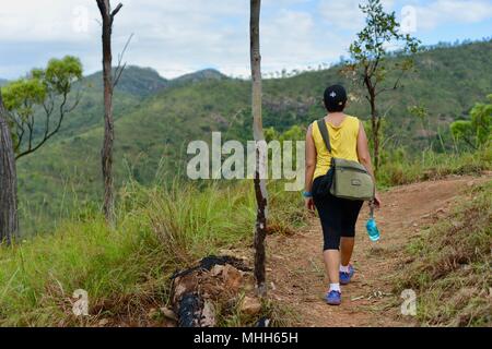 La Marche des femmes avec des vêtements de sport et une bouteille d'eau sur un chemin forestier, Mount Stuart des sentiers de randonnée, Townsville, Queensland, Australie Banque D'Images