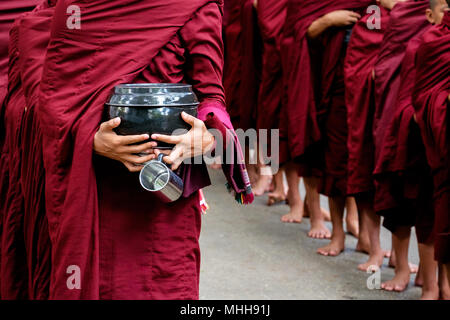 Détail de moines bouddhistes foule en robes rouges et personne tenant un bol et tasse Banque D'Images