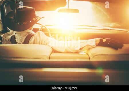 Aller à la route du soleil. Western Wear Men in Cowboy Hat classique conduite voiture décapotable. Rêve Américain Retro Style Concept. Banque D'Images