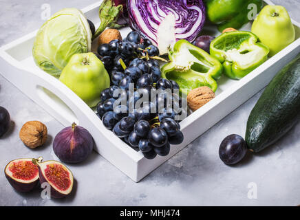 Les matières organiques fraîches de couleur violet et vert les légumes et fruits dans le bac blanc sur fond noir en foncé. Banque D'Images