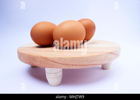 Vue de côté de trois oeufs crus sur une planche à découper en bois rond avec fond blanc Banque D'Images