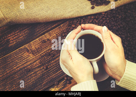 Concept de dégustation de café dans un style rustique - la femme est titulaire d'une tasse de café dans ses mains sur une table en bois avec une toile de haricots renversé sack (vi Banque D'Images