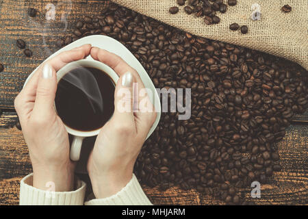 Concept de dégustation de café dans un style rustique - la femme est titulaire d'une tasse de café dans ses mains sur une table en bois avec une toile de haricots renversé sack (vi Banque D'Images