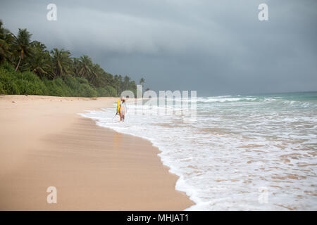 Vue arrière d'une attractive woman holding surf board dans les mains sur le littoral. Banque D'Images