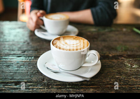 Deux tasses de café sur une table en bois, la fille tient dans sa main une tasse de café dans l'arrière-plan. Une photo indique une réunion de personnes et d'un passe-temps commun. Banque D'Images