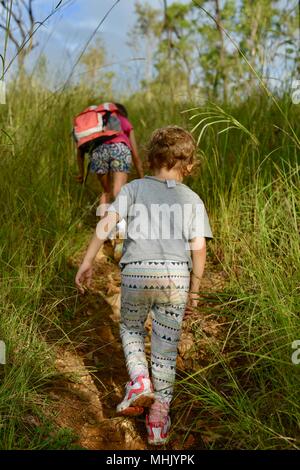 Deux enfants à monter une colline à travers l'herbe haute dans une forêt avec éclairage naturel, Mount Stuart des sentiers de randonnée, Townsville, Queensland, Australie Banque D'Images