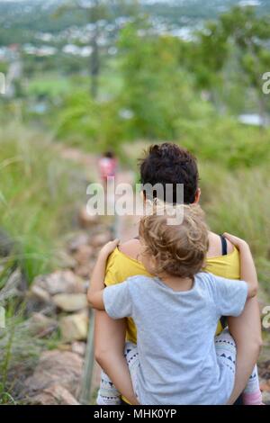 Mère portant un enfant fatigué descendre quelques marches à travers une forêt, Mount Stuart des sentiers de randonnée, Townsville, Queensland, Australie Banque D'Images