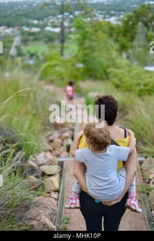 Mère portant un enfant fatigué descendre quelques marches à travers une forêt, Mount Stuart des sentiers de randonnée, Townsville, Queensland, Australie Banque D'Images