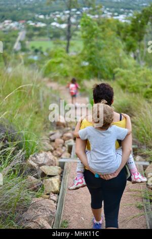 Mère portant un enfant fatigué descendre quelques marches à travers une forêt, Mount Stuart des sentiers de randonnée, Townsville, Queensland, Australie Banque D'Images