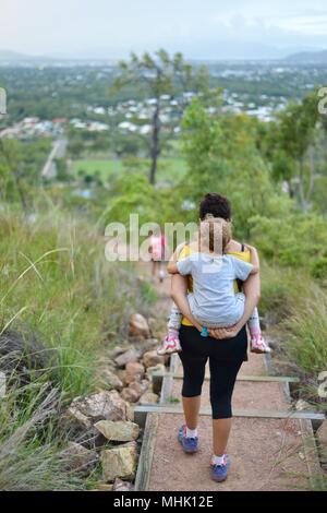 Mère portant un enfant fatigué descendre quelques marches à travers une forêt, Mount Stuart des sentiers de randonnée, Townsville, Queensland, Australie Banque D'Images