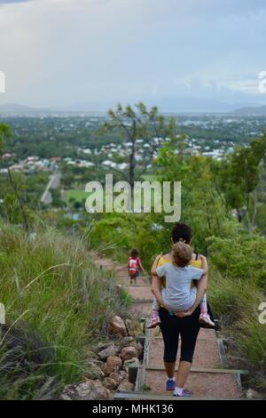 Mère portant un enfant fatigué descendre quelques marches à travers une forêt, Mount Stuart des sentiers de randonnée, Townsville, Queensland, Australie Banque D'Images