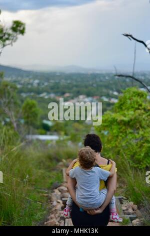 Mère portant un enfant fatigué descendre quelques marches à travers une forêt, Mount Stuart des sentiers de randonnée, Townsville, Queensland, Australie Banque D'Images