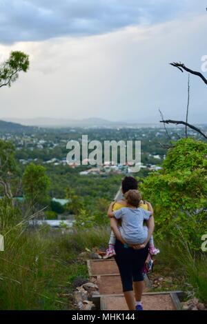 Mère portant un enfant fatigué descendre quelques marches à travers une forêt, Mount Stuart des sentiers de randonnée, Townsville, Queensland, Australie Banque D'Images