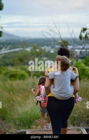 Mère portant un enfant fatigué descendre quelques marches à travers une forêt, Mount Stuart des sentiers de randonnée, Townsville, Queensland, Australie Banque D'Images