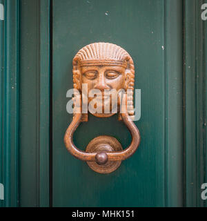 Heurtoir en laiton représentant une tête de l'Égypte ancienne sur une porte en bois vert foncé. Format carré. Banque D'Images