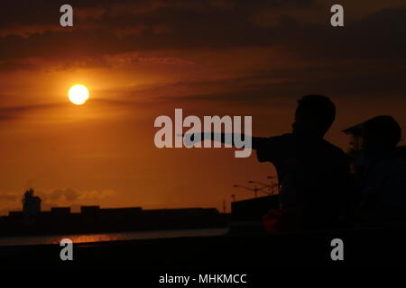 Manille, Philippines, Région de la capitale nationale. Apr 28, 2018. Les gens regardent le coucher du soleil comme il disparaît de la chaleur de la journée.un enfant à des points où le soleil peut fixer. Crédit : George Buid/ZUMA/Alamy Fil Live News Banque D'Images