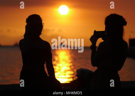 Manille, Philippines, Région de la capitale nationale. Apr 28, 2018. Les gens regardent le coucher du soleil comme il disparaît de la chaleur de la journée.Une adolescente prend une photo de son ami, avec le smartphone, comme ils attendent le coucher du soleil. Crédit : George Buid/ZUMA/Alamy Fil Live News Banque D'Images