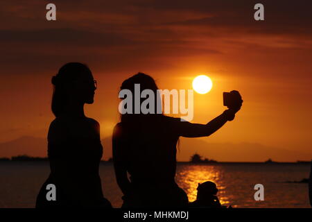 Manille, Philippines, Région de la capitale nationale. Apr 28, 2018. Les gens regardent le coucher du soleil comme il disparaît de la chaleur de la journée.Les adolescents prend un coucher de soleil sur une chaude selfies après-midi. Crédit : George Buid/ZUMA/Alamy Fil Live News Banque D'Images