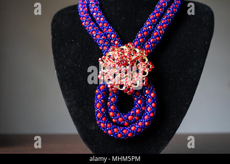 Collier artisan faite de perles rouge et bleu avec une broche d'or et d'oreilles assorties sur un mannequin noir Banque D'Images