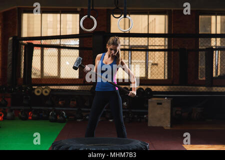 Jeune femme marteler à grand pneu sport. Jeune femme fitness sportswear en faisant l'entraînement avec chien en salle de sport. Banque D'Images