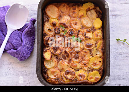 La moussaka, un plat à base de pommes de terre dans les cuisines des Balkans et de la Méditerranée/ moussaka grecque traditionnelle avec le boeuf haché et les pommes de terre sur l'onglet en bois clair Banque D'Images