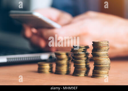 Businessman using smartphone avec pièces empilées en premier plan, gros plan avec selective focus Banque D'Images